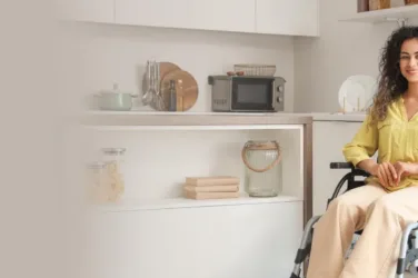 Jeune femme brune en fauteuil roulant, dans sa cuisine.