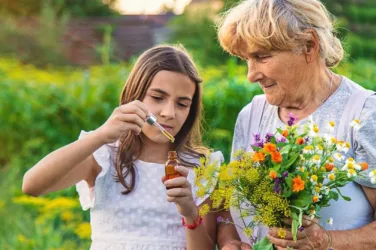 Une dame âgée tient un bouquet de fleurs des champs et sa petite fille tient un flacon d'huiles essentielles.