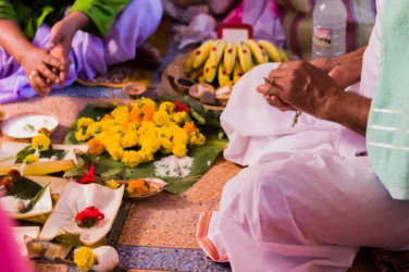 Une femme pratique un rite funéraire, assise en tailleur devant des fleurs et des offrandes.