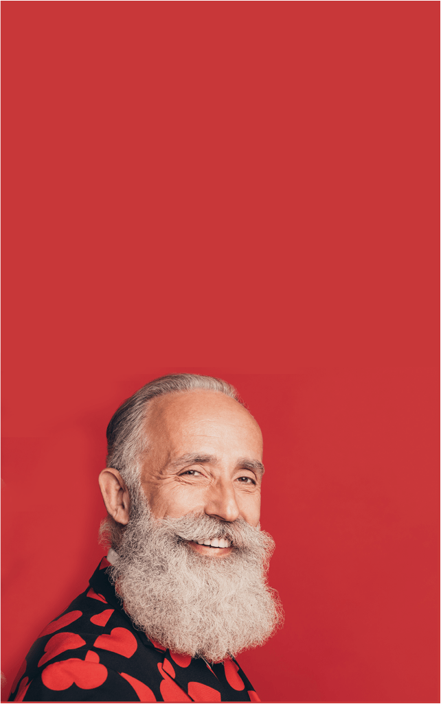 Un sexagénaire avec une barbe blanche, souriant, sur fond rouge.